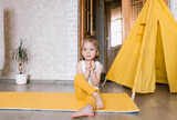 a little girl in yellow pants is doing fitness exercises on a yellow sports mat. color of the year.