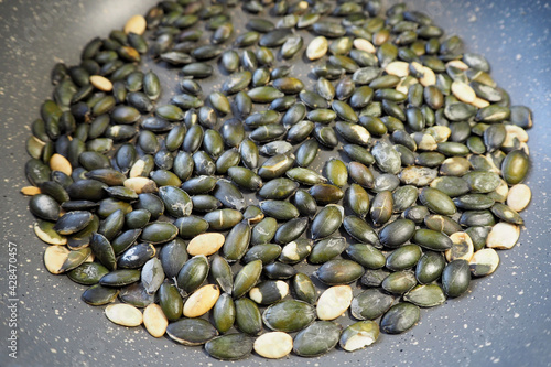 on top of the gray pan is a lot of green-colored roasted pumpkin seeds. side view . a gray frying pan on a dark table . cooking at home photo