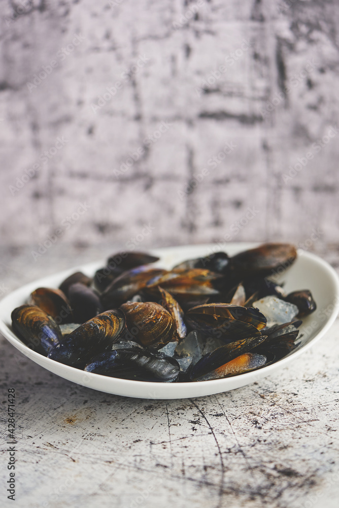 Fresh and raw sea mussels in white ceramic bowl on stone background Fresh and raw sea mussels in white ceramic bowl on stone background