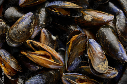 Close up shot of fresh and raw sea mussels in black ceramic bowl placed on dark