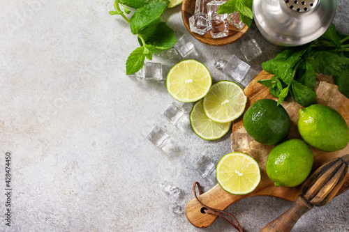 Refreshing cold summer Mojito cocktail making. Mint, lime, ice ingredients and bar utensils on a stone or concrete table. Top view flat lay. Copy space.