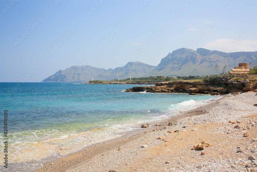 Playa de arena con el mar tranquilo un día soleado de verano con las montañas de fondo en una pequeña bahia