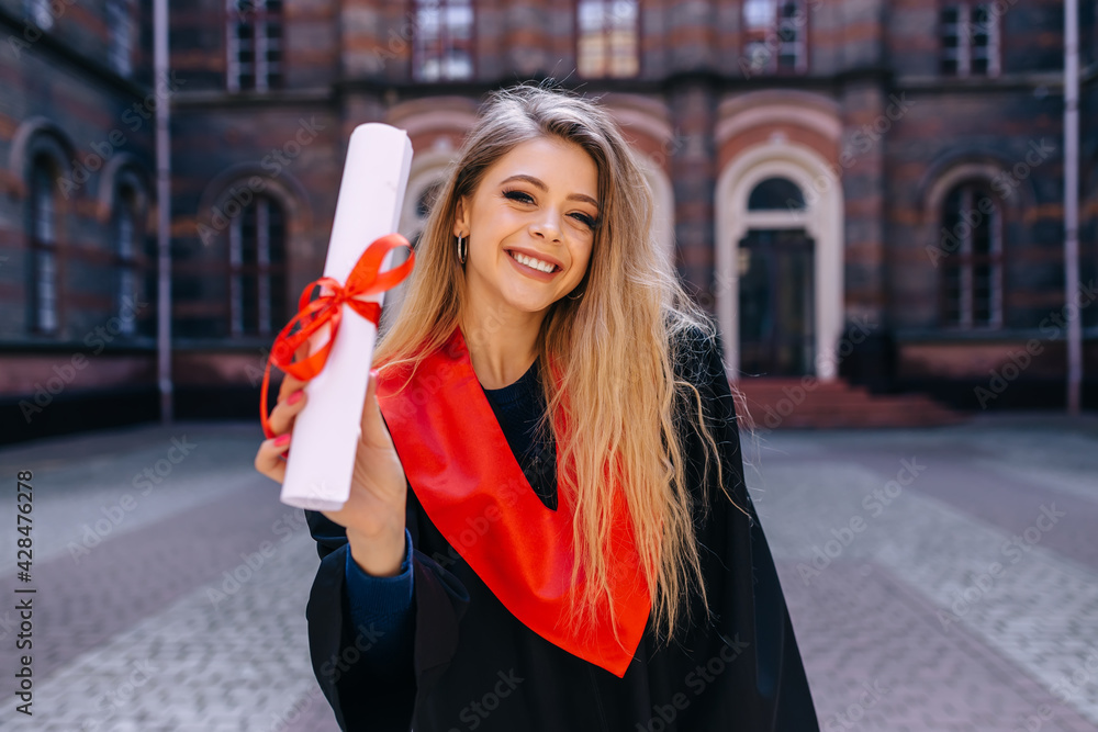 Fototapeta premium Young smiling woman holding a diploma. She is happy about the end of her studies. Congratulations to all graduates.