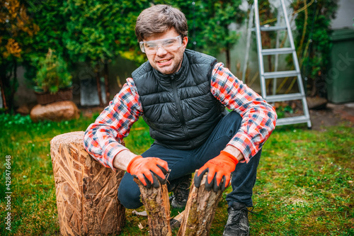 a handsome smiling man chopping a piece of wood with his hands, lumberjack in the garden