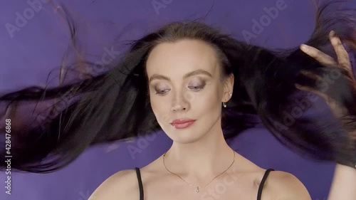 Charming beautiful cute young girl brunette model with beautiful eyes poses for camera and touches wind blowing hair on purple background in foto studio