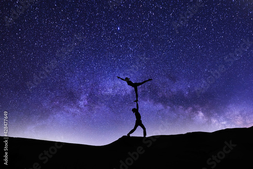 Two silhouette of a person dance in the bright starry night. Beautiful blue milky way galaxy on the sky.