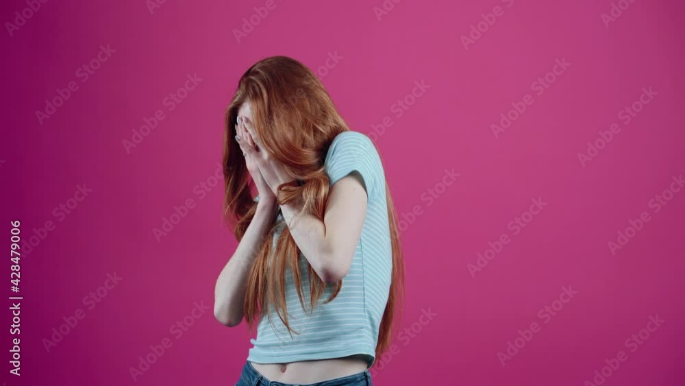 The scared redhead covers her face with her hands and then leans back scared with her hands in front of her, isolated on a pink background. The concept of people's lifestyle The scared redhead covers her face with her hands and then leans back scared with her hands in front of her, isolated on a pink background. The concept of people's lifestyle