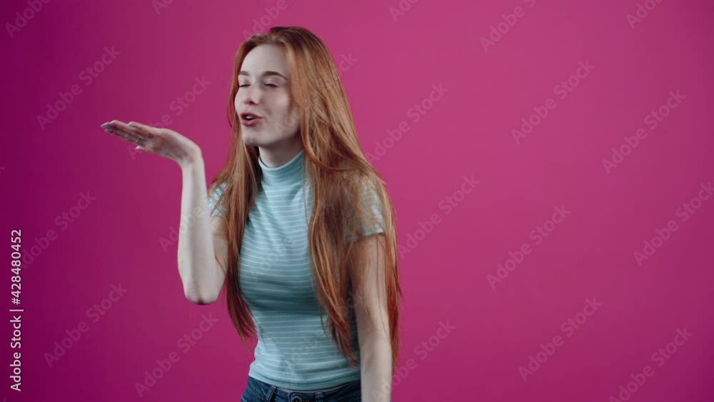 The young, optimistic redhead sends air kissing and then puts her hands on her heart as a sign of gratitude, isolated on a pink background. The concept of people's lifestyle The young, optimistic redhead sends air kissing and then puts her hands on her heart as a sign of gratitude, isolated on a pink background. The concept of people's lifestyle