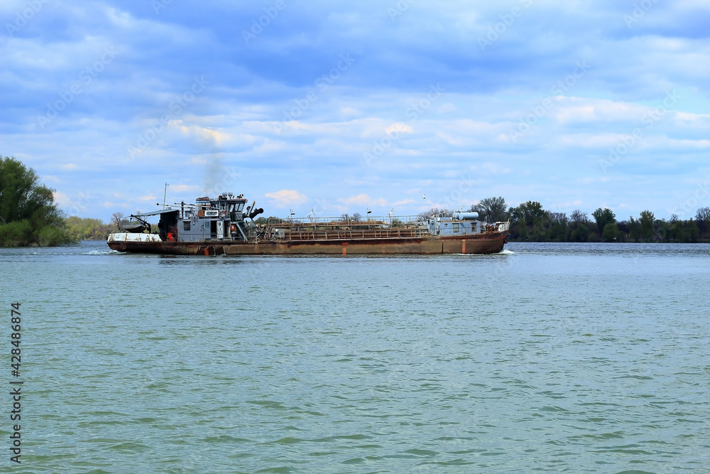 tanker on the Danube river in Belgrade with forest in the background and cloudy sky