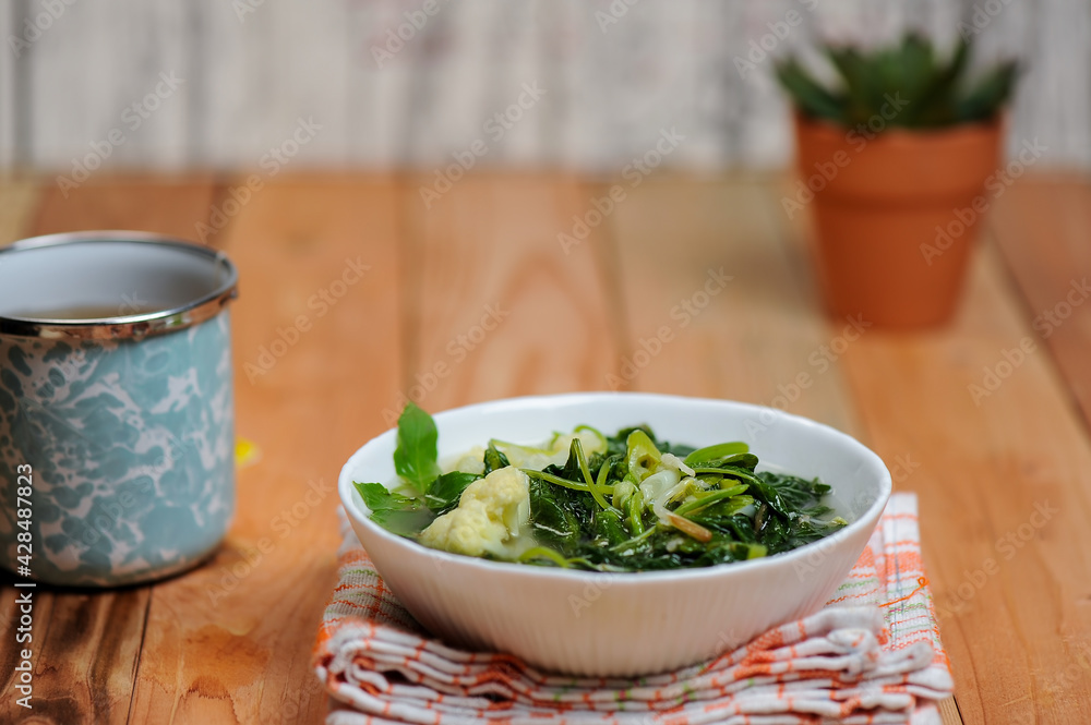 Sayur Bening Bayam or spinach clear soup with broccoli in a white bowl and wooden table Sayur Bening Bayam or spinach clear soup with broccoli in a white bowl and wooden table