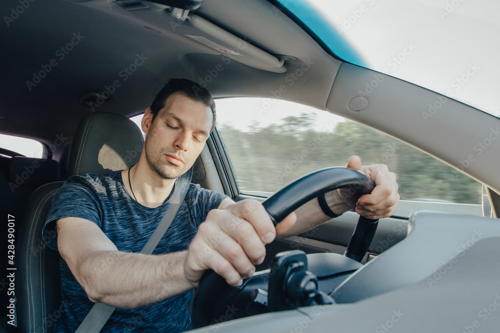 Fatigue of sleeping driver driving at speed while holding wheel while driving on highway in forest. Front view of exhausted man Fatigue of sleeping driver driving at speed while holding wheel while driving on highway in forest. Front view of exhausted man