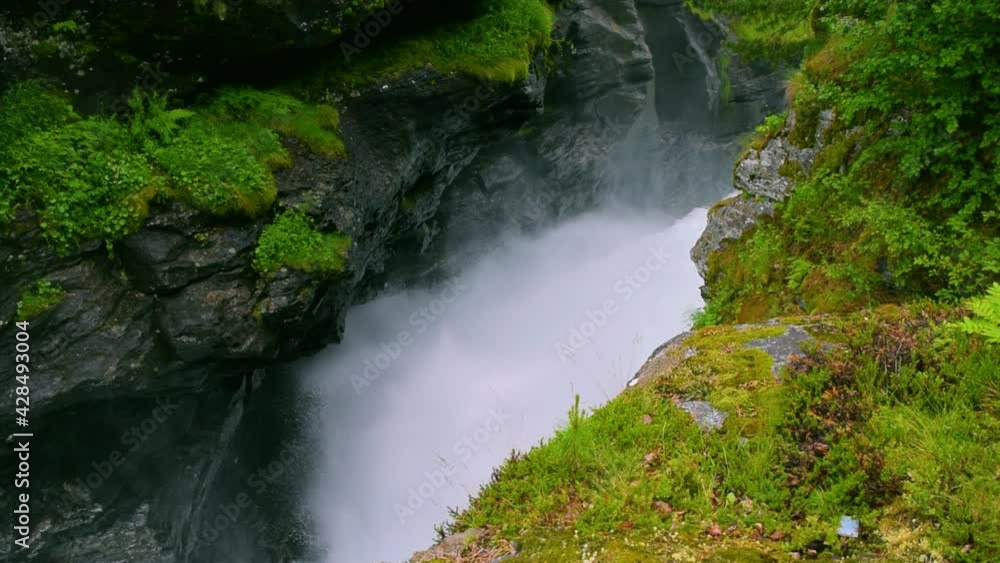Stormy streams of water of the Slettafossen waterfall, which carved a channel in the rock. Rocky summer landscape of green forest. Norway. Stormy streams of water of the Slettafossen waterfall, which carved a channel in the rock. Rocky summer landscape of green forest. Norway.