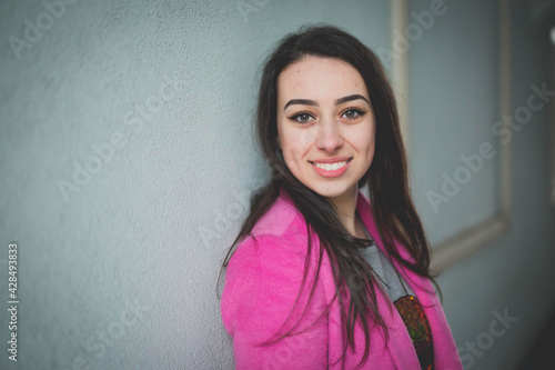 Young Caucasian female from Bosnia and Herzegovina in a pink jacket posing on a street and smili photo