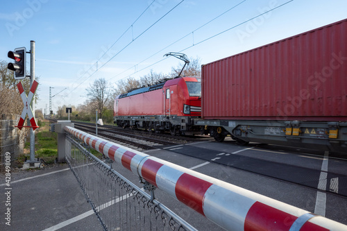 Billede på lærred Selective focus view at red and white level crossing railway barrier which block the road and locomotive of freight train move on the rail on countryside in Germany