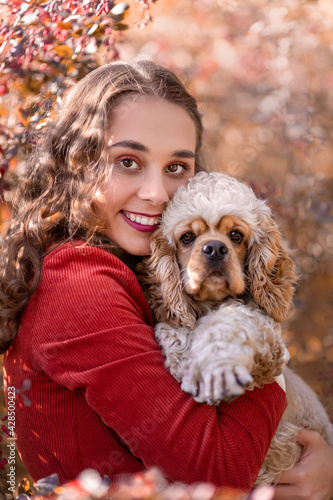 Cute young woman hugging american cocker spaniel dog at nature in park against background of autumnal leaves