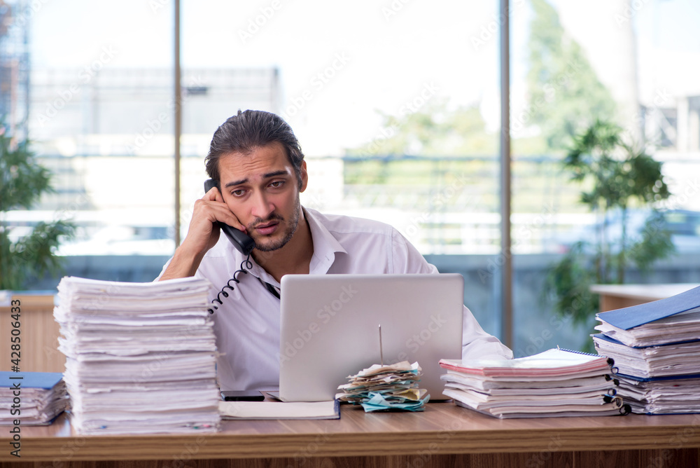 Young male employee unhappy with excessive work in the office Young male employee unhappy with excessive work in the office