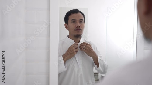 muslim asian man looking at mirror and get dressed before going to the mosque photo
