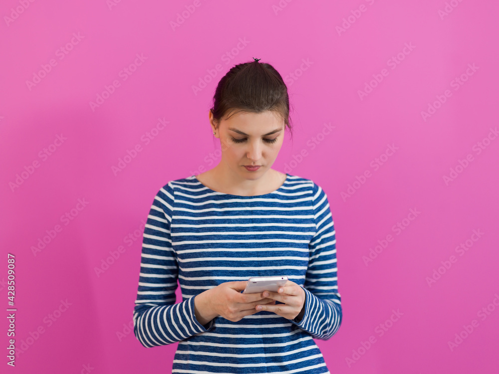 girl uses a cell phone while standing in front of a pink background girl uses a cell phone while standing in front of a pink background