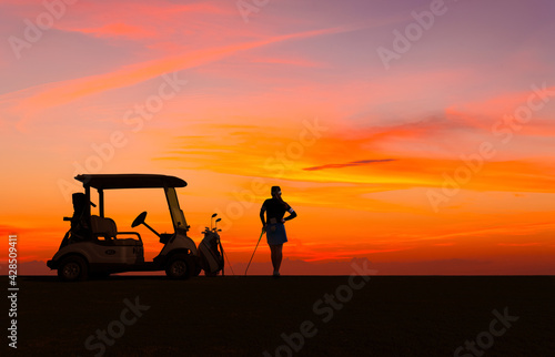 Silhouette lady golfer standing on golf course and golf cart with sun sky twilight background.