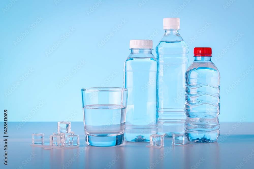 Bottles and glass of mineral water with ice cubes on blue background. Bottles and glass of mineral water with ice cubes on blue background.