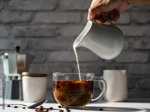 pouring cream milk into cup of coffee