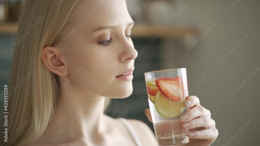 Young woman drinks water with strawberries and lemon in the kitchen. Detox drink for good health. Young woman drinks water with strawberries and lemon in the kitchen. Detox drink for good health.