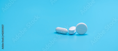Round white tablets pills and oval tablets pills on blue background. Pharmacy shop banner. Prescription drugs. Pharmaceutical industry. Painkiller, antibiotics, and antacid tablet pills. Pharmaceutic. photo