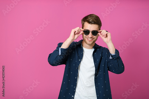 a portrait of a young man wearing a blue shirt and posing in front of a pink background 