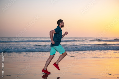Sporty man runner running in summer beach, colorful sunset sky. © Volodymyr
