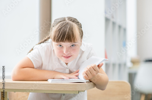 Young girl with syndrome down reads a book at school. Education for disabled children concept photo