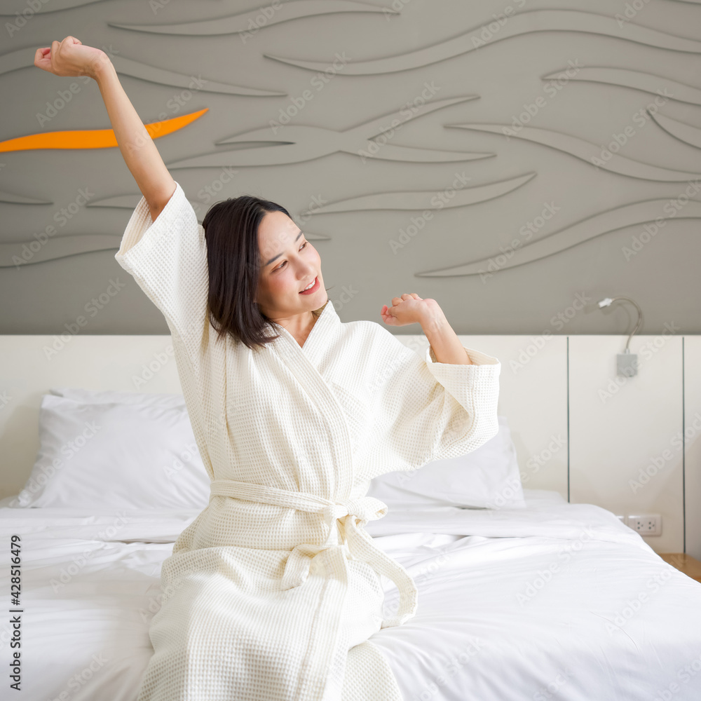 Asian woman in bathrobe rest on vacation, sitting in bed at home. Stretch after get up in the morning Asian woman in bathrobe rest on vacation, sitting in bed at home. Stretch after get up in the morning