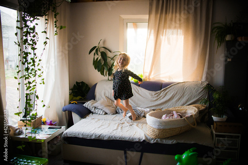 A little girl indulges on the couch at home next to her younger newborn sister. High quality photo
