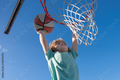 Closeup portrait of kid boy basketball player making slam dunk during basketball game.