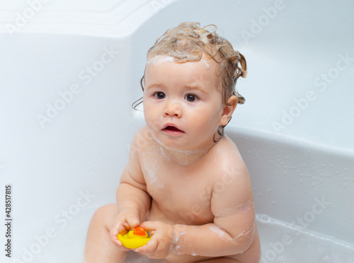 Funny baby bathes in bathtub with water and foam. Kids hygiene. Little child in a bathtub. Smiling kid in bathroom with toy duck.