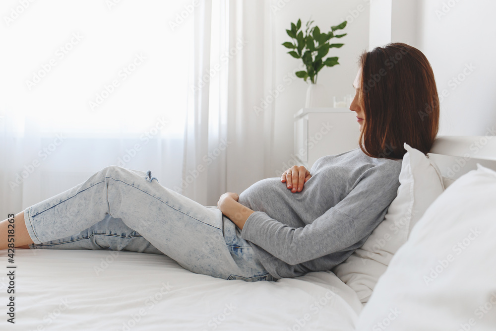 Young beautiful pregnant woman lying on bed with white linen. Young beautiful pregnant woman lying on bed with white linen.
