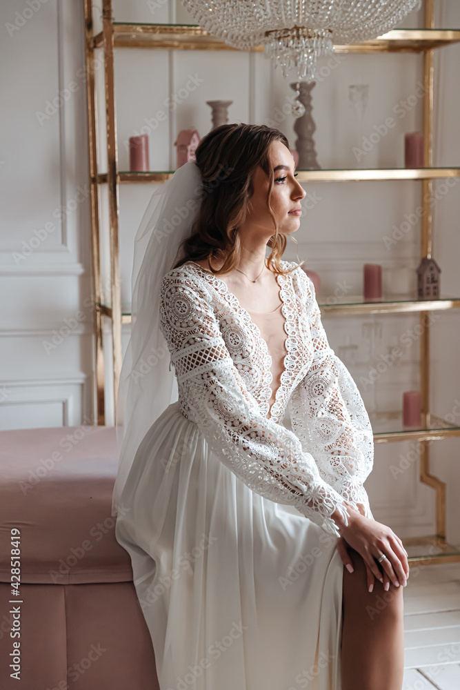 Portrait of a young bride in a lace wedding dress in a cozy interior.