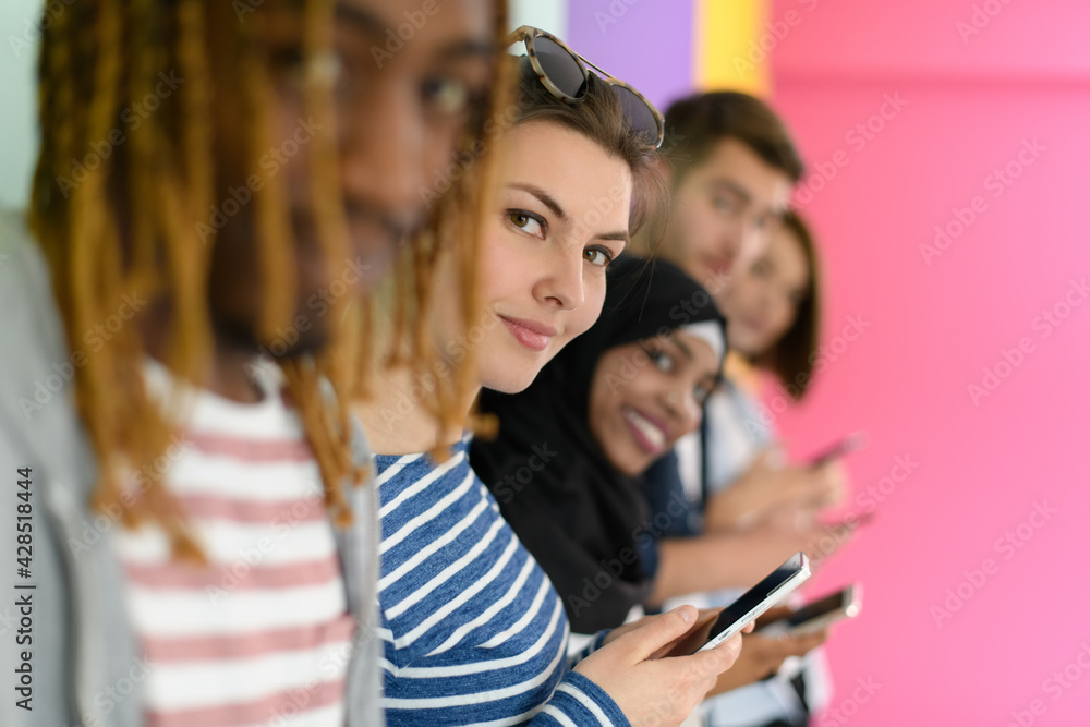 diverse teenagers use mobile devices while posing for a studio photo in front of a pink background diverse teenagers use mobile devices while posing for a studio photo in front of a pink background