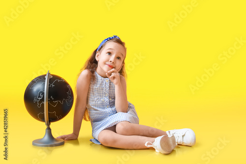 Thoughtful little girl with globe on color background