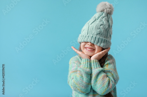 Stylish little girl in winter clothes on color background