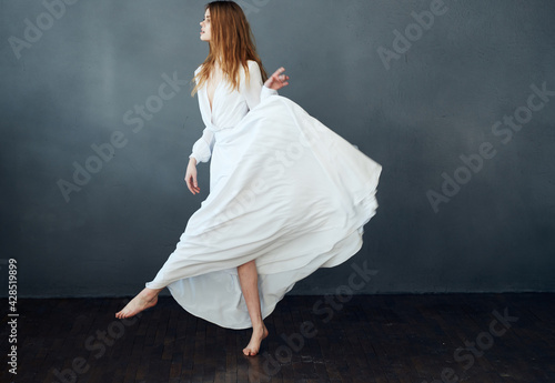 Beautiful woman in a white dress to the floor on a gray background in full growth