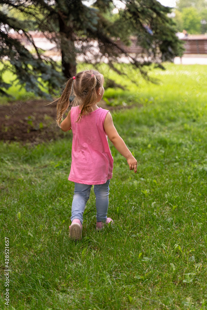 a little girl in a pink tunic walks on the grass in sneakers a little girl in a pink tunic walks on the grass in sneakers