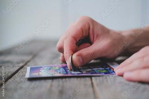 A man is hand erases a protective field in a lottery with a coin on a wooden background. Won. Gambling, addiction. 