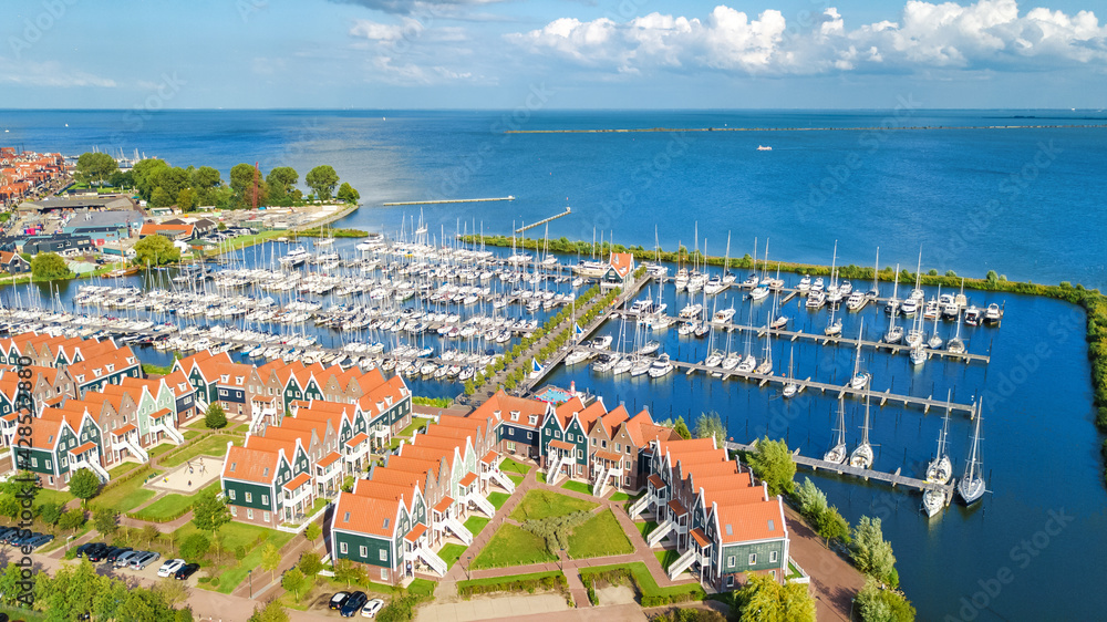 Aerial drone view of typical modern Dutch houses and marina in harbor from above, architecture of port of Volendam town, North Holland, Netherlands
