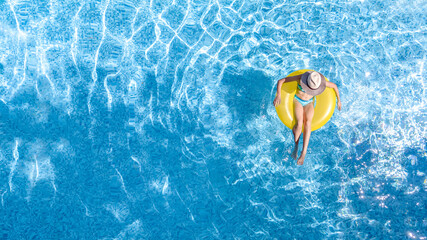 Active young girl in swimming pool aerial top view from above, child relaxes and swims on inflatable ring donut and has fun in water on family vacation, tropical holiday resort
