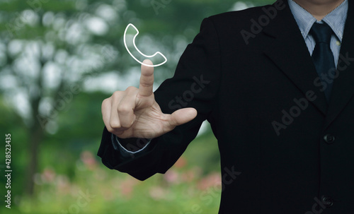 Businessman pressing telephone flat icon over blur flower and tree in park, Business contact us, Customer service and support concept