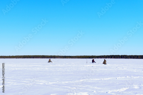 fishermen sit fishing on a winter lake against a background of forest and blue sky. sports winter fishing