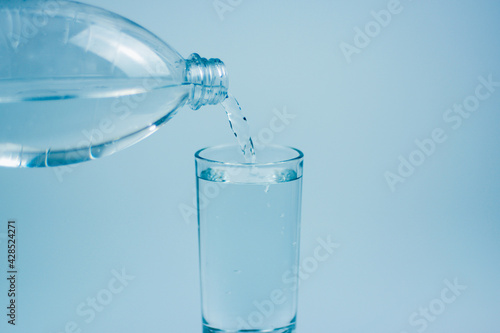 Pouring water into glass on light blue background.