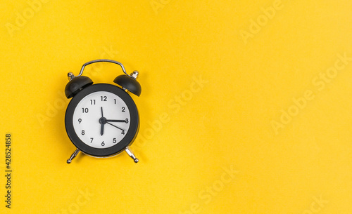 black alarm clock on yellow background. copy space. flat lay