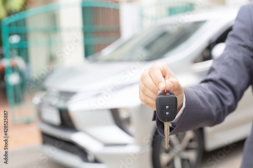 A woman holds a car key in front of a car in a showroom.