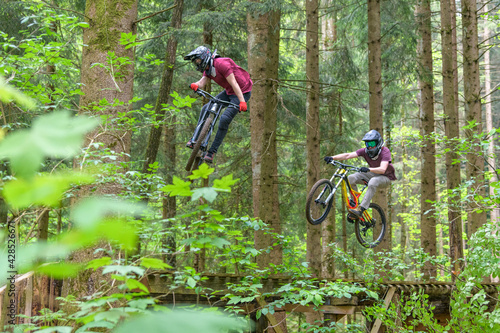 Tollkühne Mountainbiker springen gemeinsam über eine Rampe im Wald